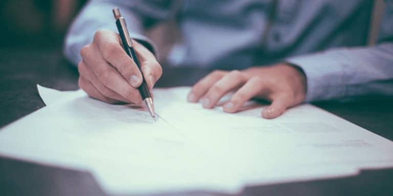 Persona firmando documento legal para liquidar herencia con cuaderno particional.