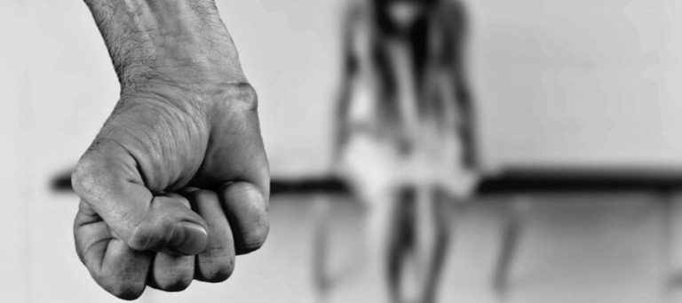 Imagen de un puño cerrado en primer plano, con una mujer en el fondo en un entorno judicial.