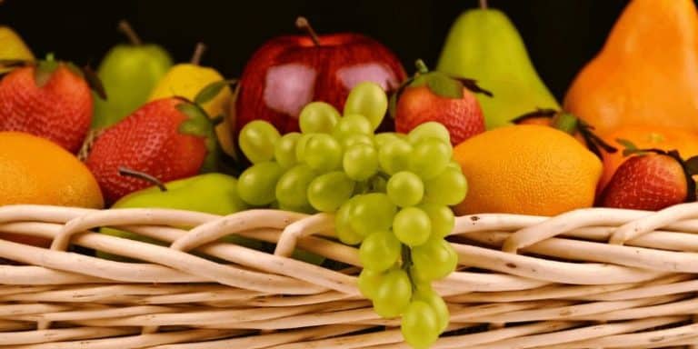 Alimentos en una cesta, incluyendo frutas variadas como uvas, manzanas, naranjas y peras.