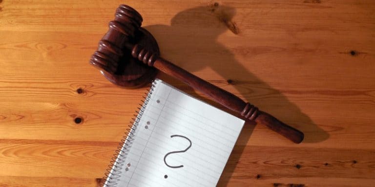 Martillo de juez y nota con signo de interrogación sobre mesa de madera.