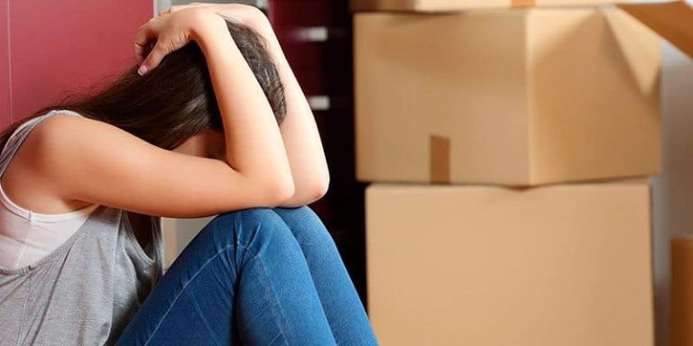 Mujer triste con cajas de mudanza, reflejando inseguridad tras separación.