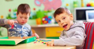 Niños jugando en aula educativa con juguetes y materiales didácticos.
