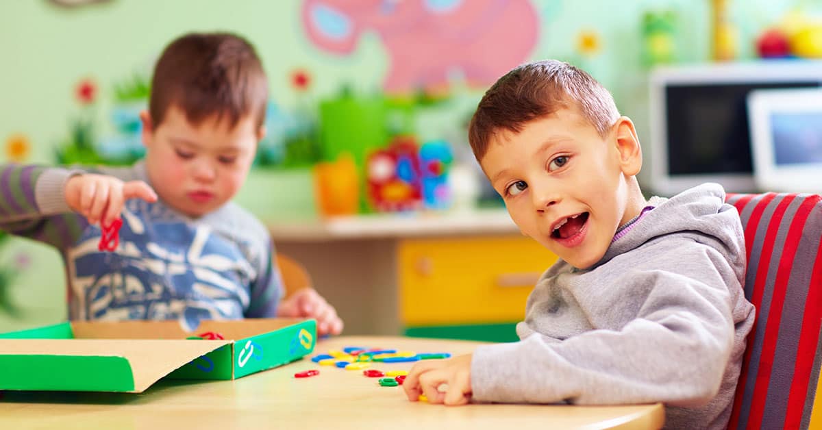 Niños jugando en aula educativa con juguetes y materiales didácticos.
