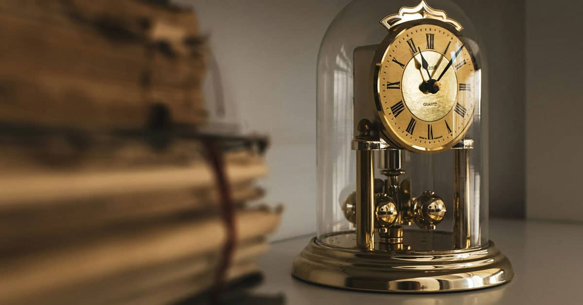 Reloj de sobremesa vintage con péndulo dorado, en una mesa junto a libros apilados.