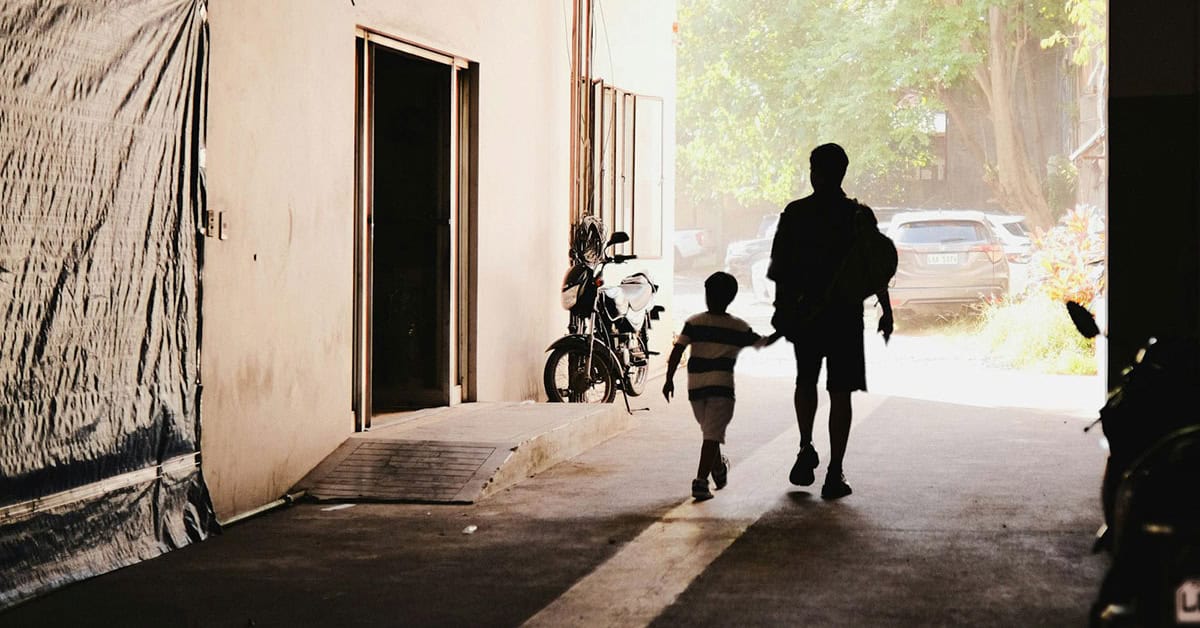 Caminando con un niño en un pasaje urbano, en un entorno con luz natural y vehículos estacionados.