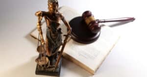 Figura de la Justicia con balanza y martillo en un fondo de libro y pluma.