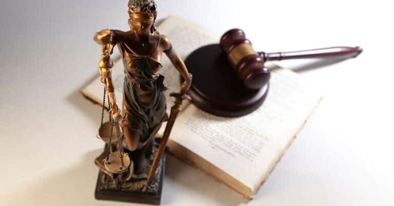 Figura de la Justicia con balanza y martillo en un fondo de libro y pluma.