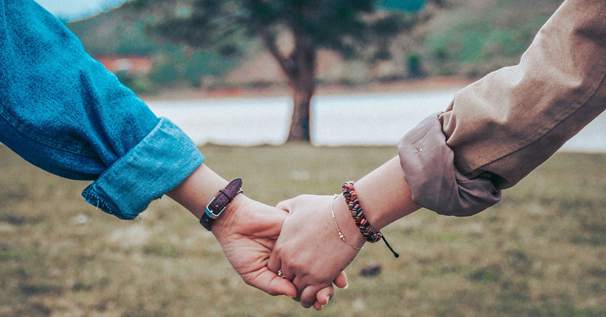 Amor y amistad entre dos personas tomadas de la mano en un entorno natural al aire libre.