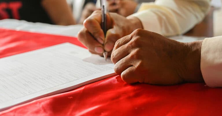 Persona firmando un acuerdo matrimonial en una mesa con documentos.