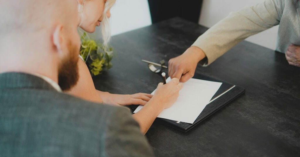 Personas firmando documentos de capitulaciones matrimoniales en una oficina.