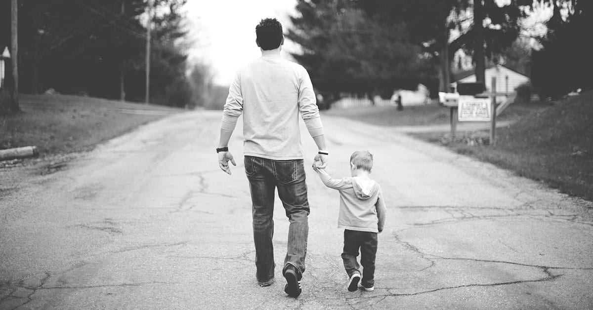 Padre e hijo caminando de la mano en la calle en un día soleado.