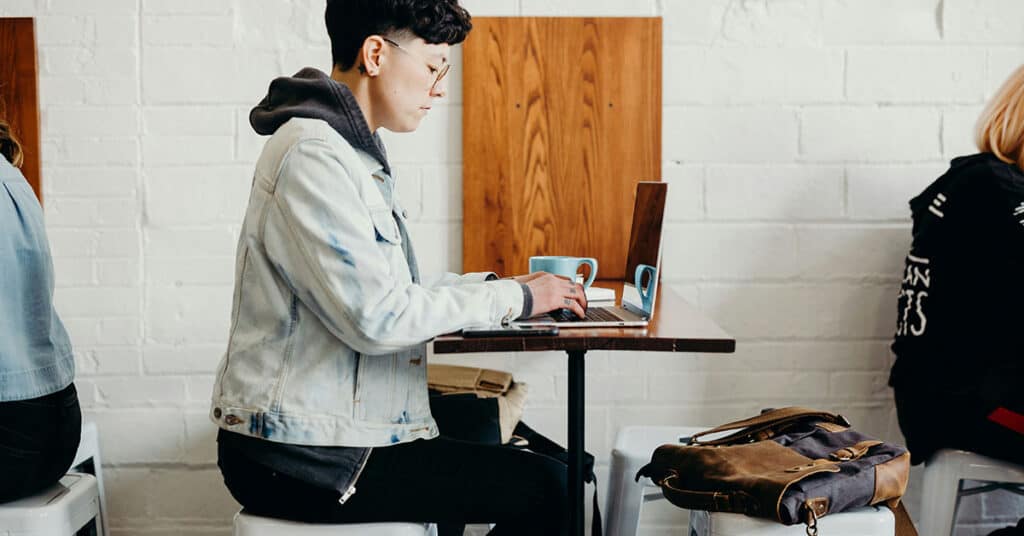 Joven estudiando con laptop y café en un espacio moderno.