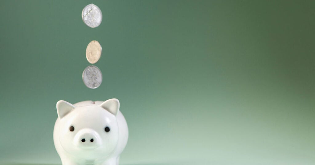 Cerdito de cerámica con monedas en caída para ahorro y pensión.