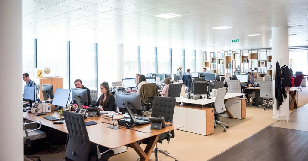 Oficina moderna con empleados en escritorios con computadoras y estanterías.