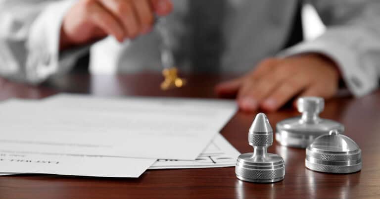 Persona firmando documentos legales con sellos y pluma en oficina.