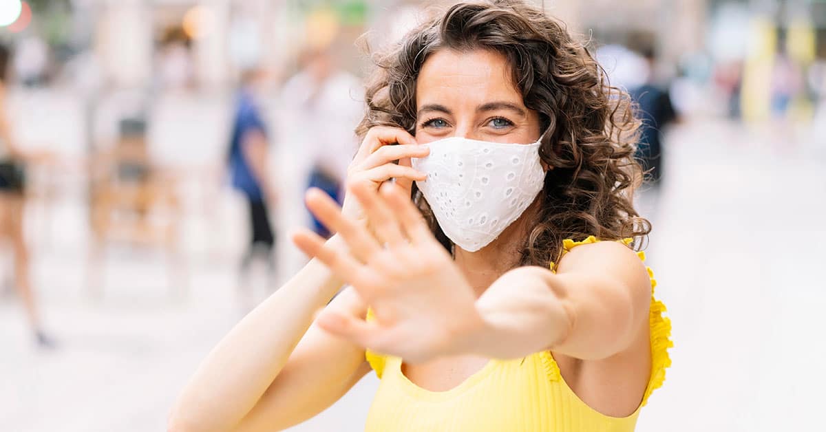 Mujer sonriente con mascarilla en espacio público, salud y protección.