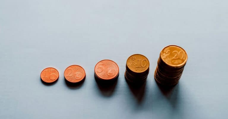 Monedas de diferentes valores en orden ascendente sobre fondo azul claro.