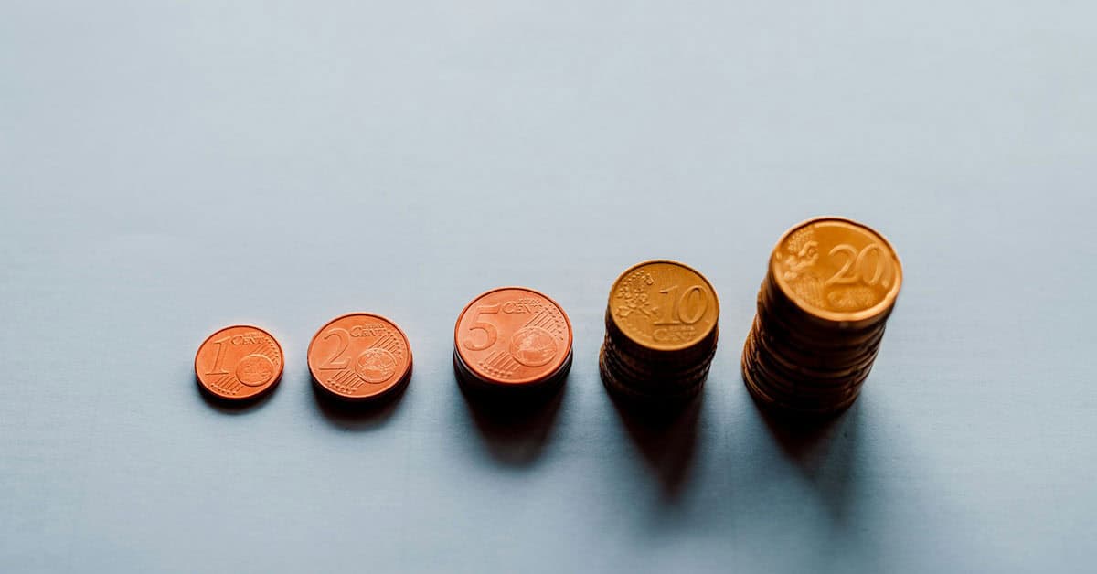 Monedas de diferentes valores en orden ascendente sobre fondo azul claro.